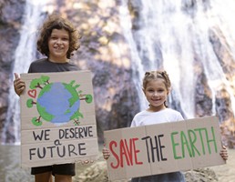 Two young girls, standing in front of a waterfall, holding handmade signs "save the earth" and "we deserve a future" 