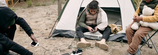 A family living in a tent charging phones and tablets outside
